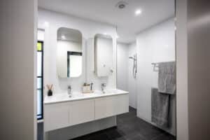 Modern bathroom with double sinks, large mirrors, a walk-in shower, and gray towels hanging on a towel rack.